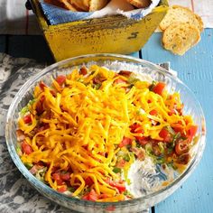 a bowl filled with cheese and vegetables next to some crackers on a table top