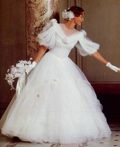 a woman in a white wedding dress is holding her hand out to the side while wearing gloves