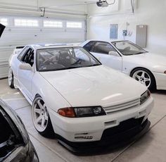 two white cars parked in a garage next to each other with their hoods open