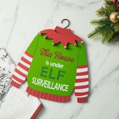 this house is under elf surveillance ornament on a marble table with christmas decorations