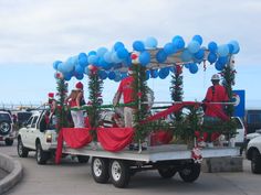 two men in red and white outfits are riding on a truck with balloons attached to the back