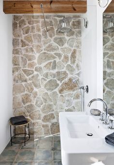 a bathroom with stone walls and flooring next to a white sink under a mirror