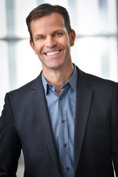 a man in a suit smiling at the camera with his hands on his hips and wearing a blue shirt