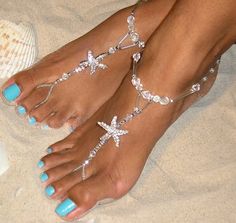 a woman's feet with jewelry on them and seashells in the background