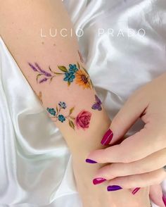 a woman's arm with flowers on it and purple nail polishes in the foreground