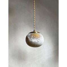 a round stone hanging from a rope on a gray wall with white clouds in the background