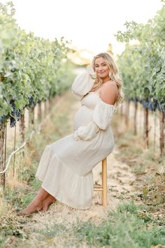 a pregnant woman sitting on a chair in the middle of a vineyard