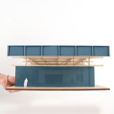 a hand holding a model of a building made out of blue corrugated sheets and wooden planks