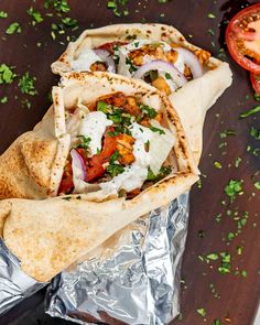 two burritos sitting on top of aluminum foil next to tomatoes and parsley