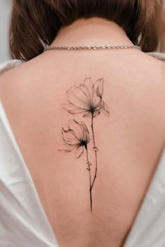 the back of a woman's neck with a single flower tattoo on her left shoulder