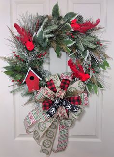 a christmas wreath hanging on the front door with red and green ribbons, evergreens, pine cones and birdhouse