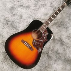 an acoustic guitar sitting on top of a white carpeted floor with a black and orange cover