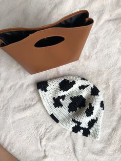 a crocheted cow print hat next to a brown purse on a white blanket