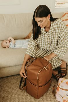 a woman sitting on the floor next to a baby in a diaper changing bag