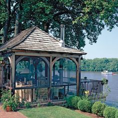 a gazebo sitting on top of a lush green field next to a lake with boats in the water