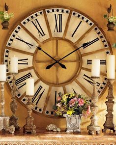 a large clock sitting on top of a mantle next to candles and vase filled with flowers