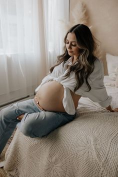 a pregnant woman sitting on top of a bed with her stomach exposed and looking down