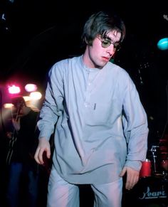 a man with sunglasses on standing in front of a drum set and lights behind him