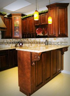 a kitchen with wooden cabinets and marble counter tops, lights above the sink and an island