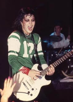 a man with long hair playing an electric guitar in front of a group of people