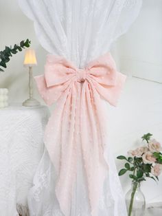 a pink bow tied to the side of a white curtain next to a vase with flowers