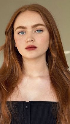 a woman with long red hair and blue eyes is looking at the camera while wearing a bra