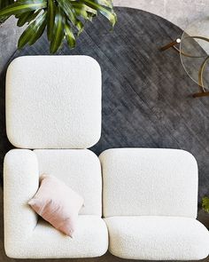 a white couch sitting next to a green plant on top of a wooden table with a pink pillow