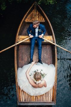 a bride and groom in a rowboat on the water with their hands up to each other