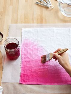 a person is painting on a piece of paper with paintbrushes and some other items