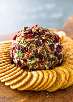 a cheese ball with nuts and cranberries on top of crackers sitting on a wooden table