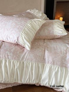 a bed with pink and white comforter next to a lit candle on the floor