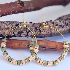 a pair of hoop earrings with green and beige beads on them sitting next to a branch