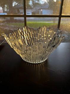 a glass bowl sitting on top of a wooden table next to a window with the sun shining through it