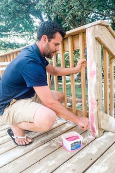 a man painting the side of a wooden deck with pink paint and a white box