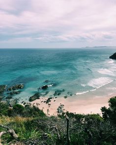 an ocean view from the top of a hill looking down on a sandy beach and clear blue water