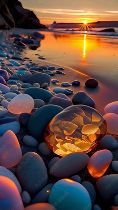 the sun is setting over some rocks on the beach with water in the foreground