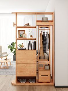 an open closet with clothes and shoes on shelves next to a plant in a living room