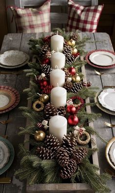 a wooden table topped with lots of candles and pine cones covered in christmas decorations next to plates