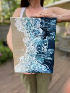 a woman holding up a piece of art that looks like waves crashing on the beach