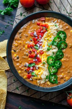 a bowl filled with beans, cheese and green peppers next to tortilla chips