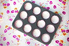 white cupcakes in a muffin tin on a floral tablecloth