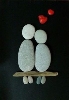 two pebbles sitting on top of a wooden board with hearts floating above them