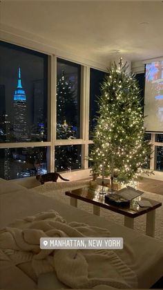 a living room with a christmas tree in the corner and large windows overlooking city lights