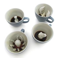 four coffee mugs with mushrooms in them on a white surface, one is filled with liquid and the other two are empty