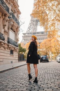 a woman standing in front of the eiffel tower wearing a black dress and hat