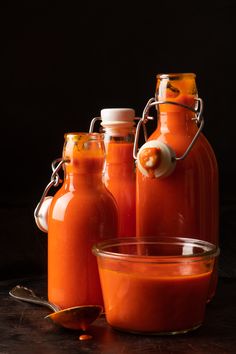 there are three bottles with hot sauce in them and one is filled with orange liquid