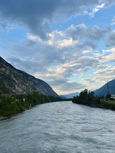 a river flowing through a lush green valley under a cloudy sky with mountains in the background