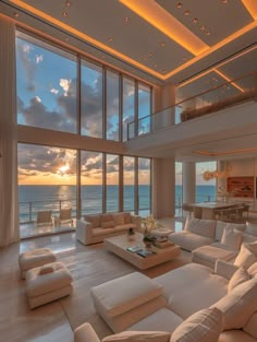 a living room filled with white furniture and large windows overlooking the ocean at sunset or dawn