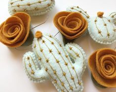 several felt cactus ornaments are arranged on a white surface with gold pins and thread in the middle