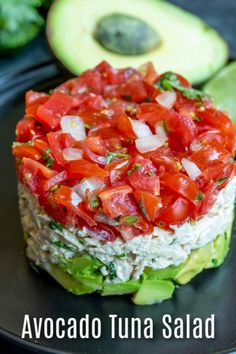 an avocado tuna salad with tomatoes and cucumbers on a black plate